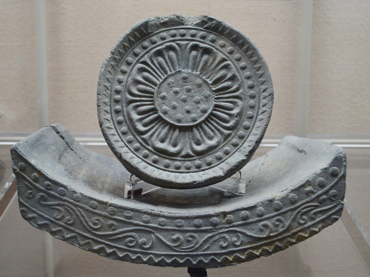 A circular lotus-pattern eave tile displayed above a curved, patterned flat eave tile.