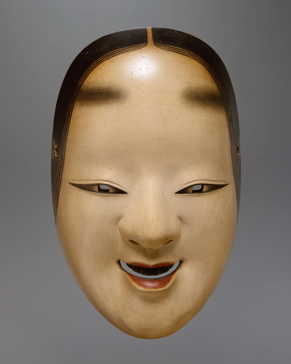 A carved ko-omote Noh mask with a pale face, fine eyebrows, and a slightly open mouth.