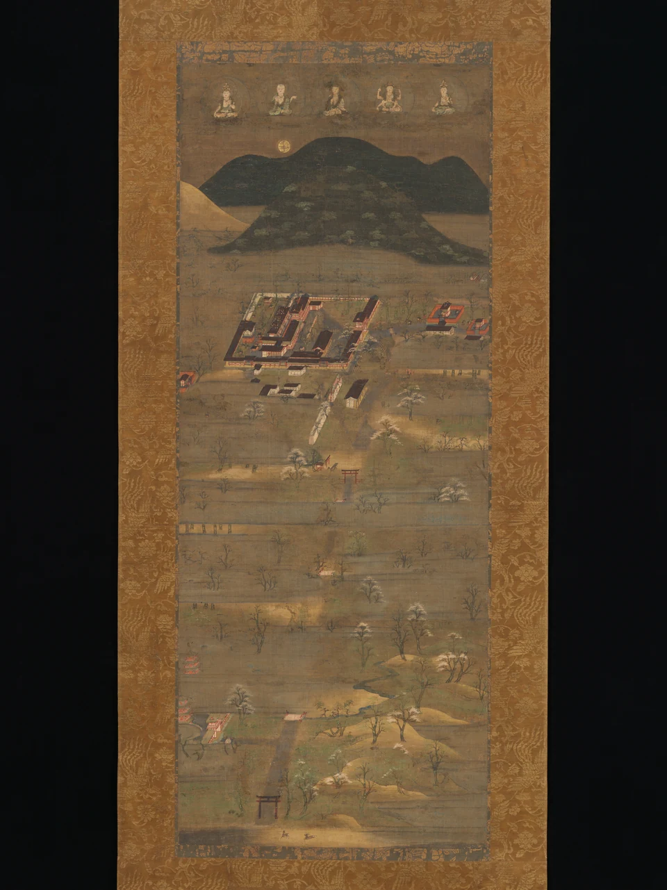 Five Buddhist figures sit above a wooded mountain in a tall painted scroll. Below, shrine buildings, gateways and an approach are arranged in a sacred landscape.