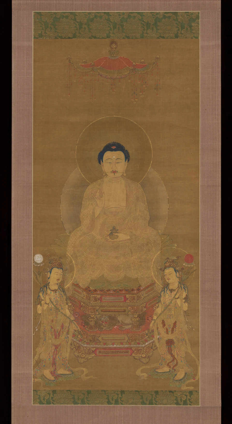 A large seated golden Medicine Buddha holds a small jar; two smaller standing attendants carry moon and sun emblems below, under a canopy.