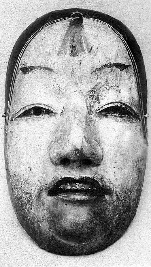 A black-and-white photograph shows a weathered Noh mask with narrow eyes, painted brows, dark hairline and a slightly open mouth.
