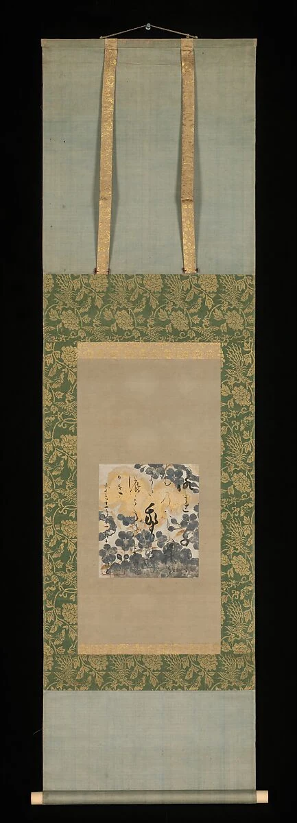 A small decorated poem card is mounted within a much taller hanging scroll with broad patterned and plain borders, a hanging cord and a bottom roller.