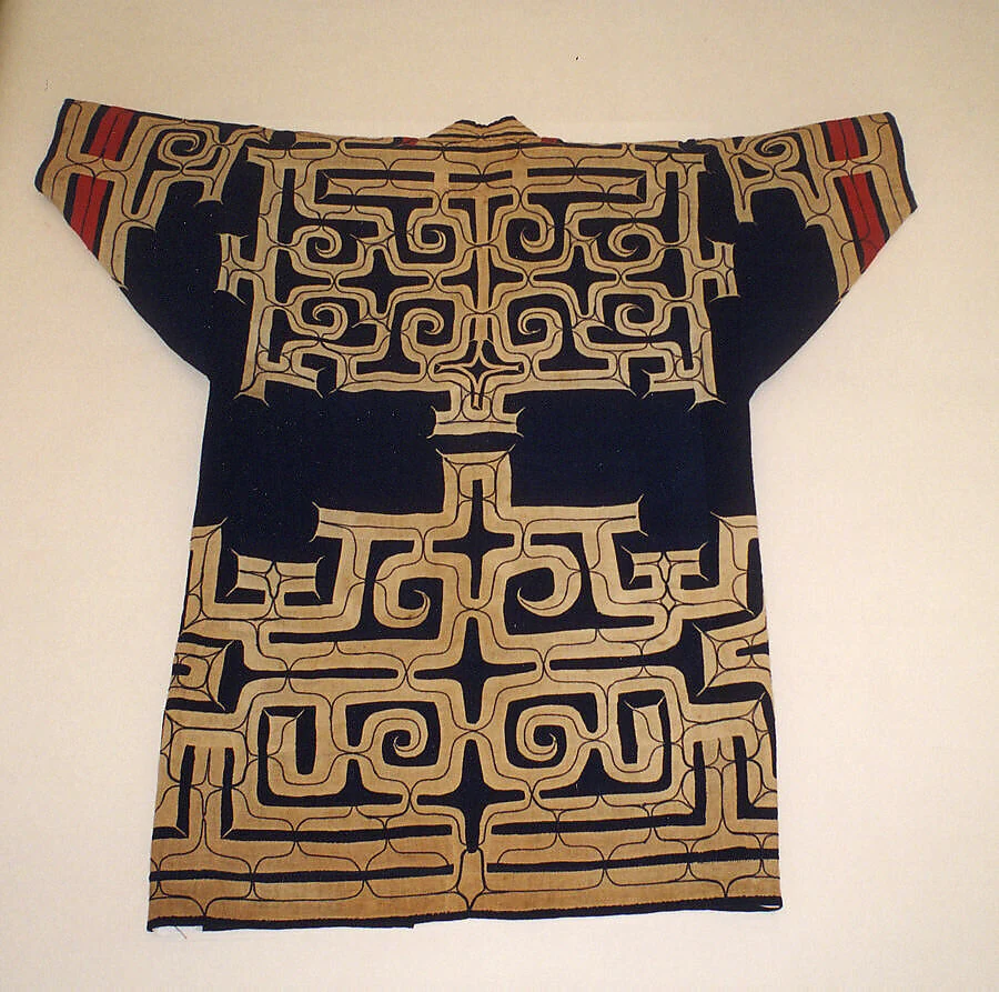 Back of a nineteenth-century Ainu cotton robe: pale applied cloth and fine curving stitched lines form large symmetrical patterns on a dark ground, with red and patterned accents near the sleeves.
