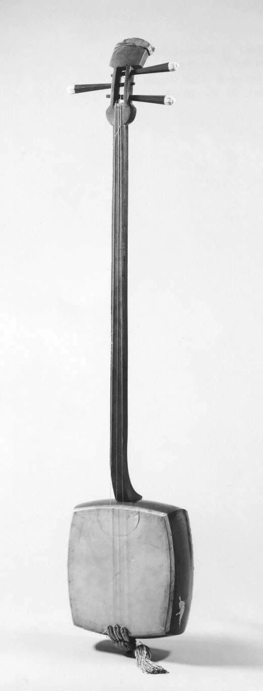 A nineteenth-century shamisen has three tuning pegs, a long narrow neck, a skin-covered roughly rectangular body and a string tie below.