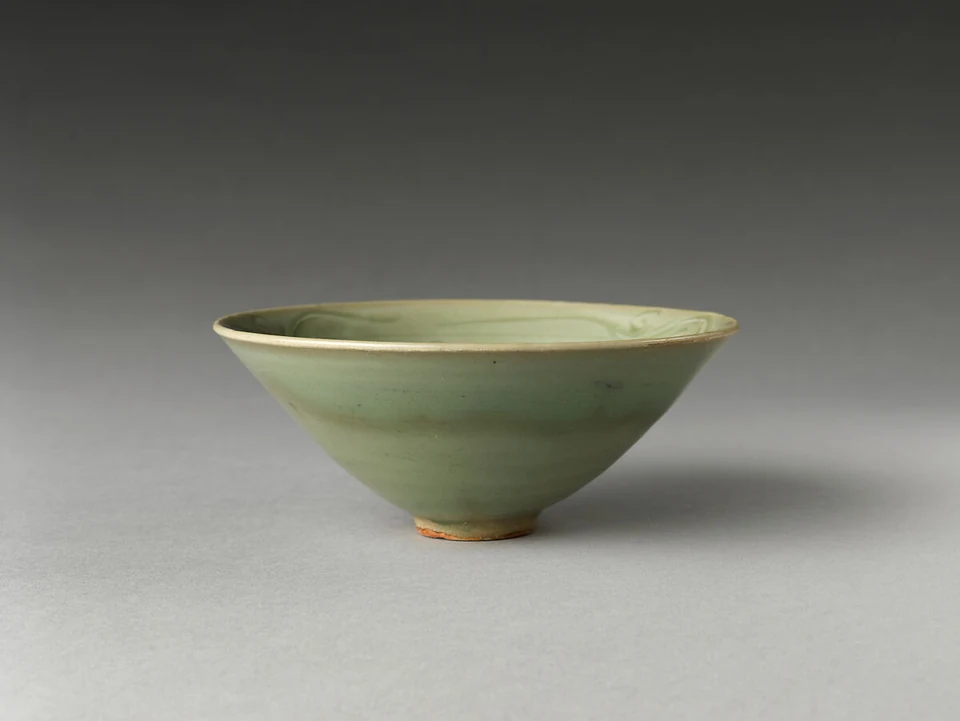 A pale green-glazed bowl has a flaring rim, a low foot with exposed clay, and incised decoration visible inside.
